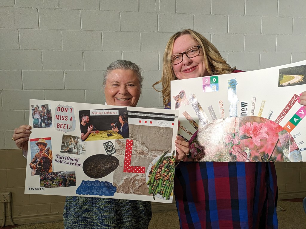 Two white women hold vision boards of collaged items up to the camera, they are both smiling softly